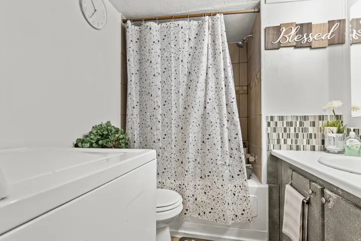 Full bathroom featuring a shower-tub combination with natural stone tile surround, a white porcelain toilet, and a vanity with a white countertop and rectangular undermount sink