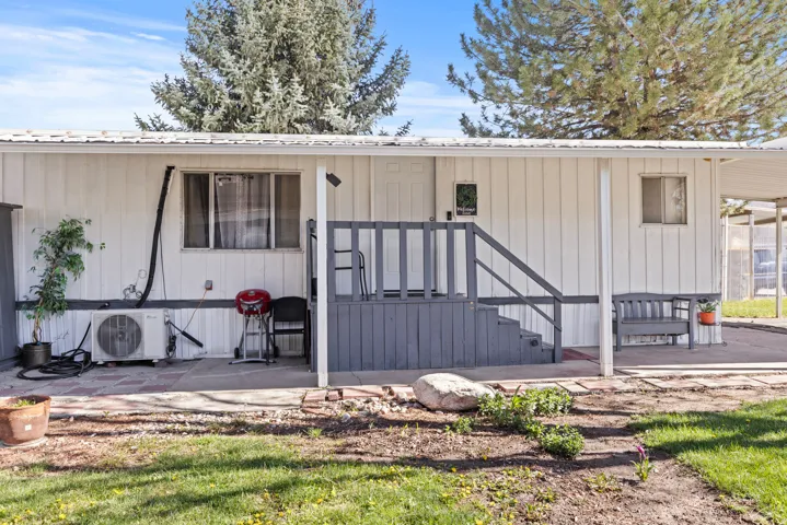 Exterior featuring white vertical siding with dark trim, a covered porch with dark wood stairs and railing, and a built-in outdoor bench