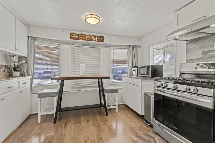 Kitchen featuring wood-finish flooring, white cabinetry, integrated stainless steel range with overhead hood, and a light-toned tile backsplash