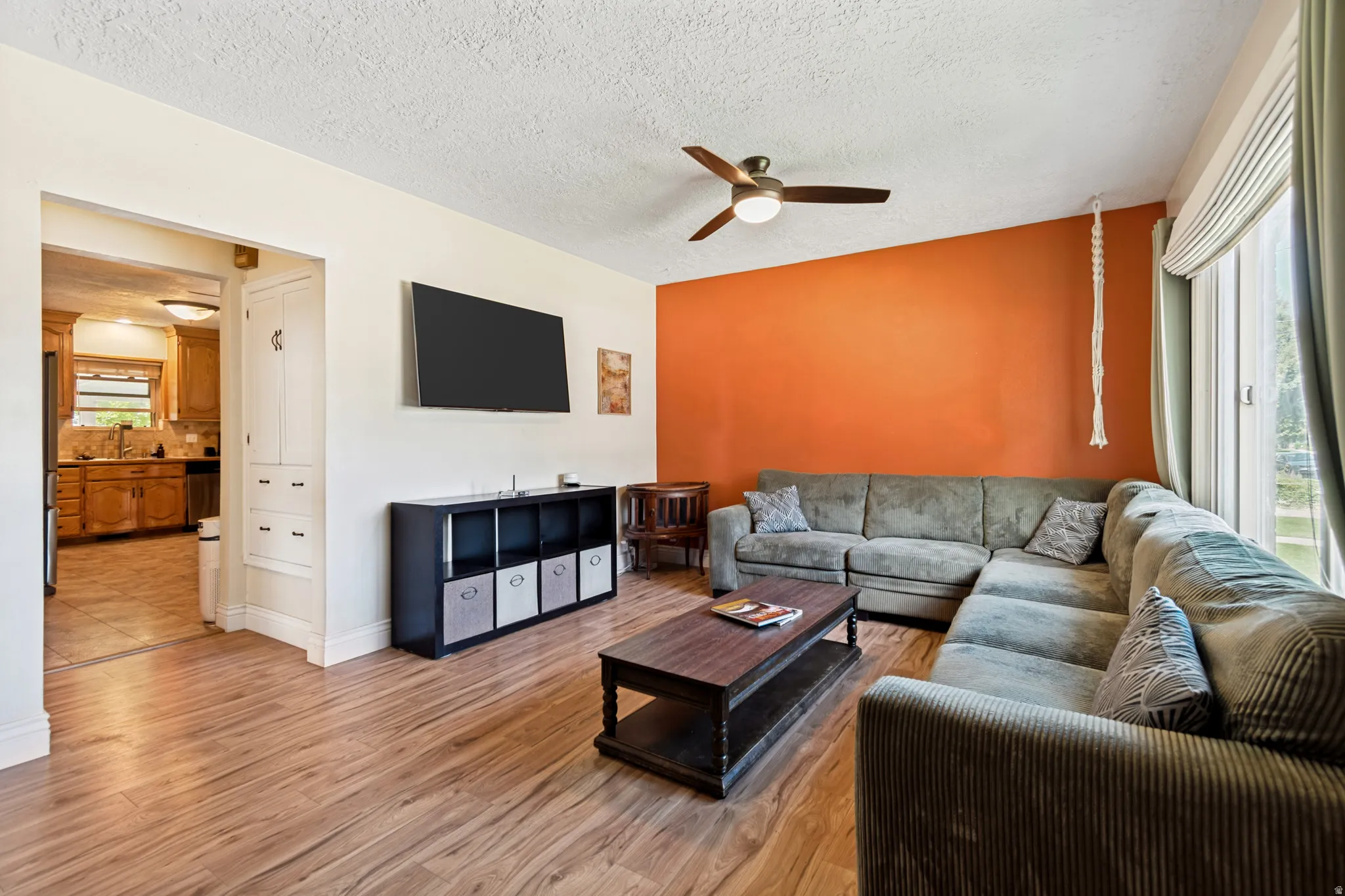 Living area featuring wood flooring, a ceiling fan with integrated lighting, and a large window with blinds