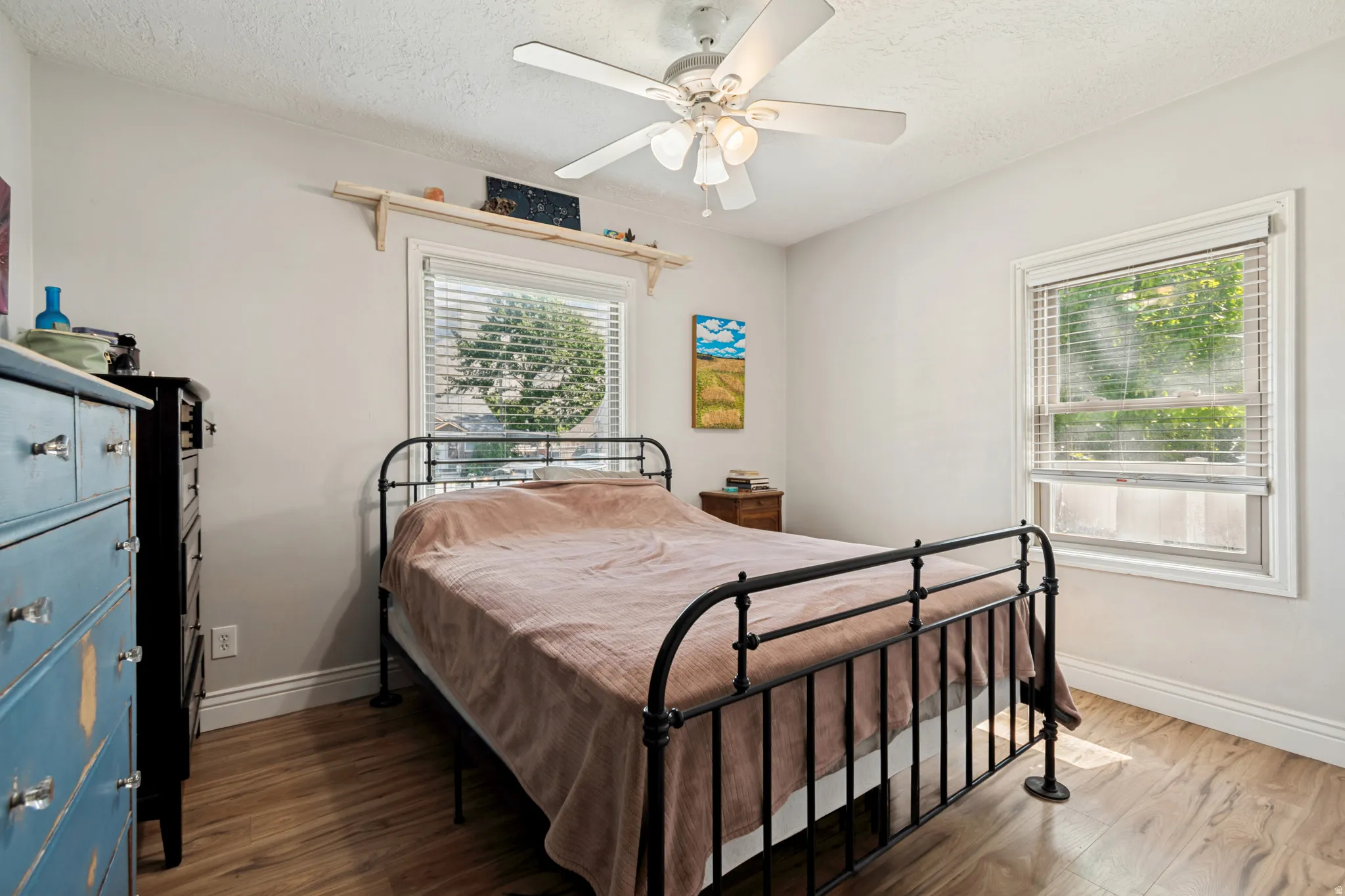 Bedroom featuring two windows with white blinds, wood flooring, and a ceiling fan with integrated lighting