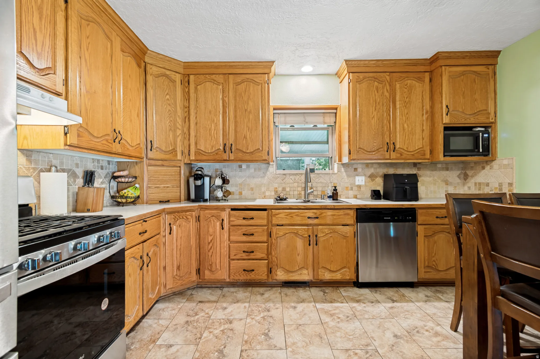 Kitchen featuring wood cabinetry, stainless steel appliances, a tile backsplash, light countertops, and tile flooring