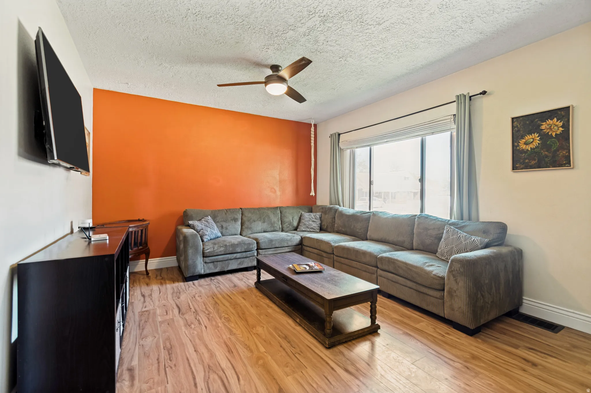 Spacious room featuring wood flooring, a contemporary ceiling fan, and a large window with drapes
