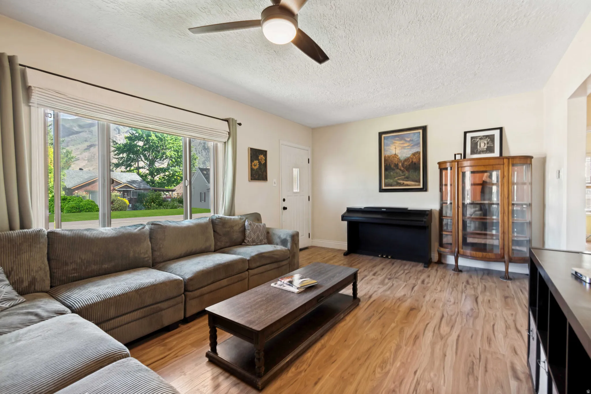 Bright living area featuring wood flooring, a large picture window, and a ceiling fan with integrated lighting