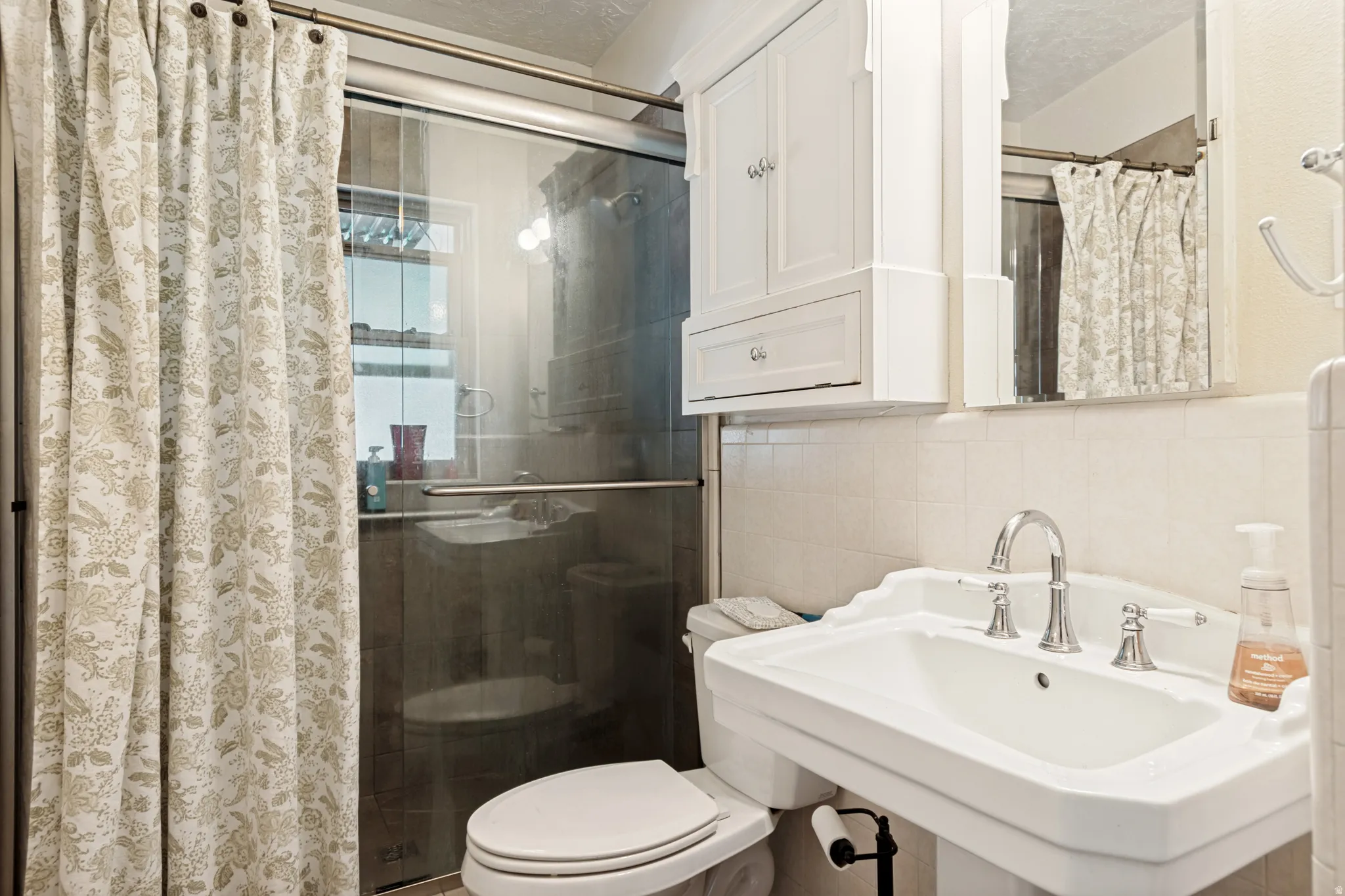 Bathroom featuring a framed glass walk-in shower, pedestal sink with chrome fixtures, a mirrored medicine cabinet, and a white storage cabinet