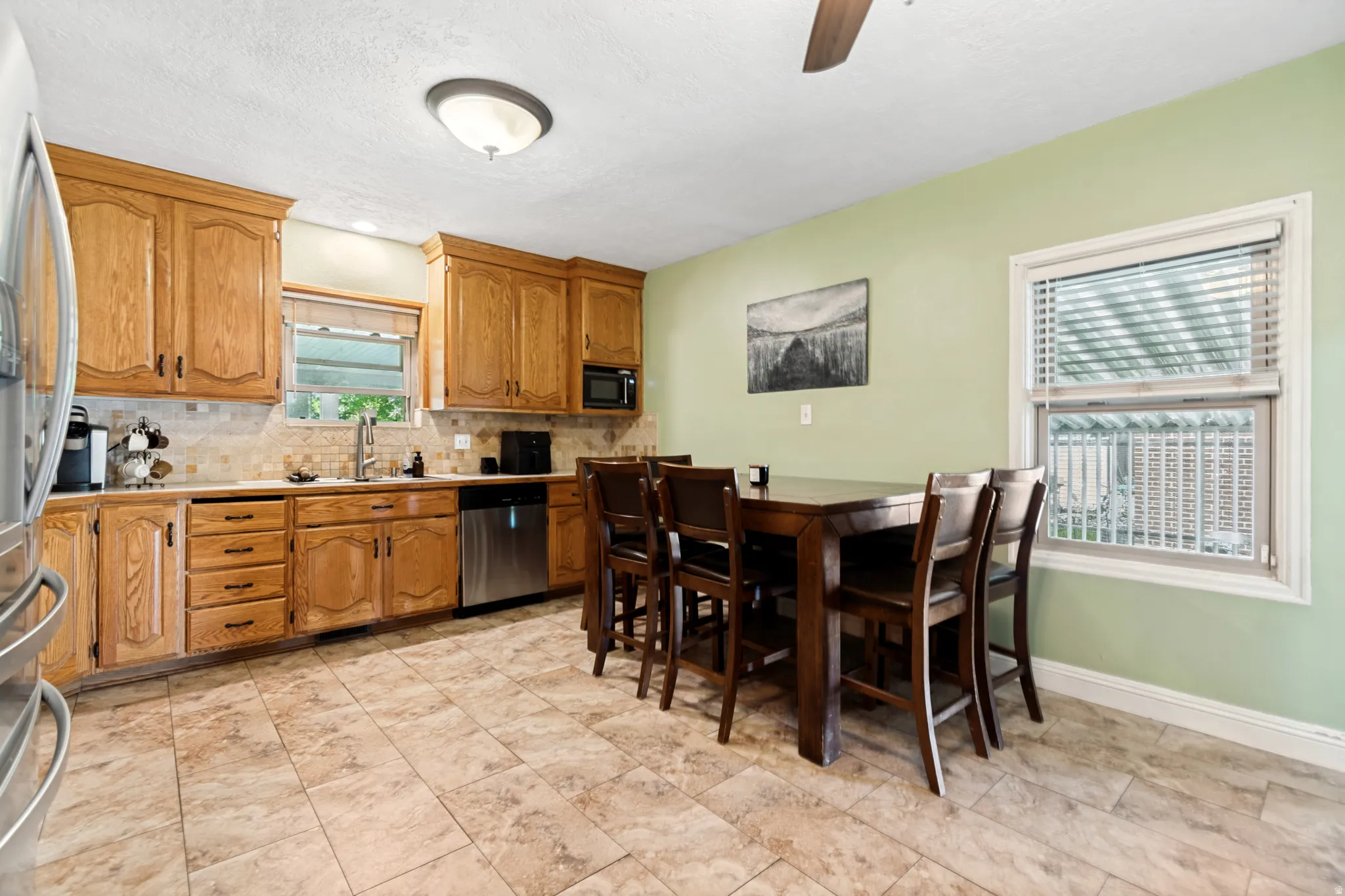 Kitchen featuring wood cabinetry, stainless steel appliances, tile backsplash, and tile flooring