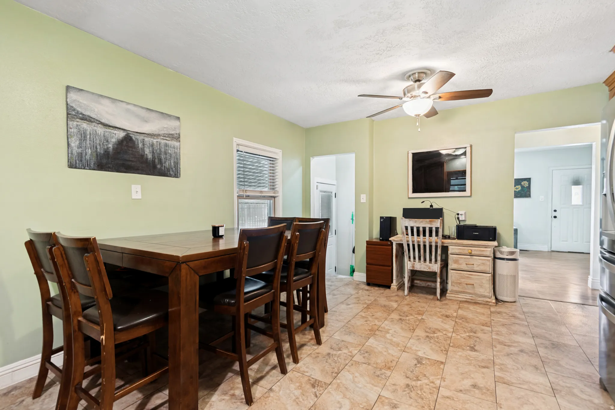 Spacious dining area featuring neutral tile flooring, light green wall paint, a ceiling fan with integrated lighting, and a white framed window with horizontal blinds