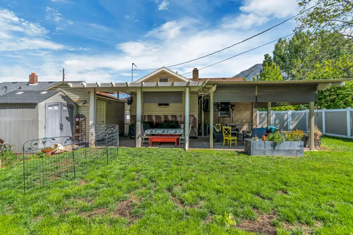 Expansive backyard featuring a covered patio, a separate storage shed, a pergola-style structure, and a wood-slat privacy fence