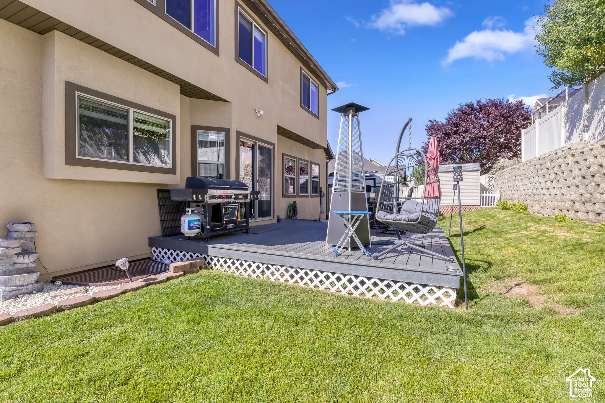 Rear exterior featuring a composite deck with white lattice skirting, direct access via sliding glass doors, a manicured lawn, and a retaining wall