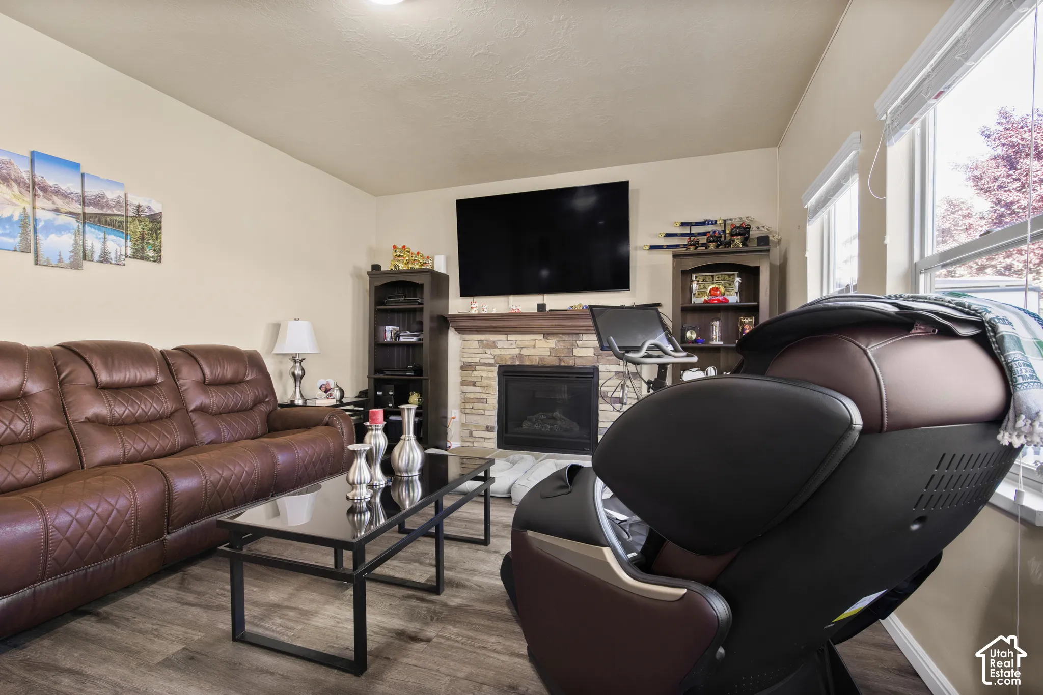 Living area featuring wood-finish flooring, a stone-faced fireplace with a mantel, and recessed lighting