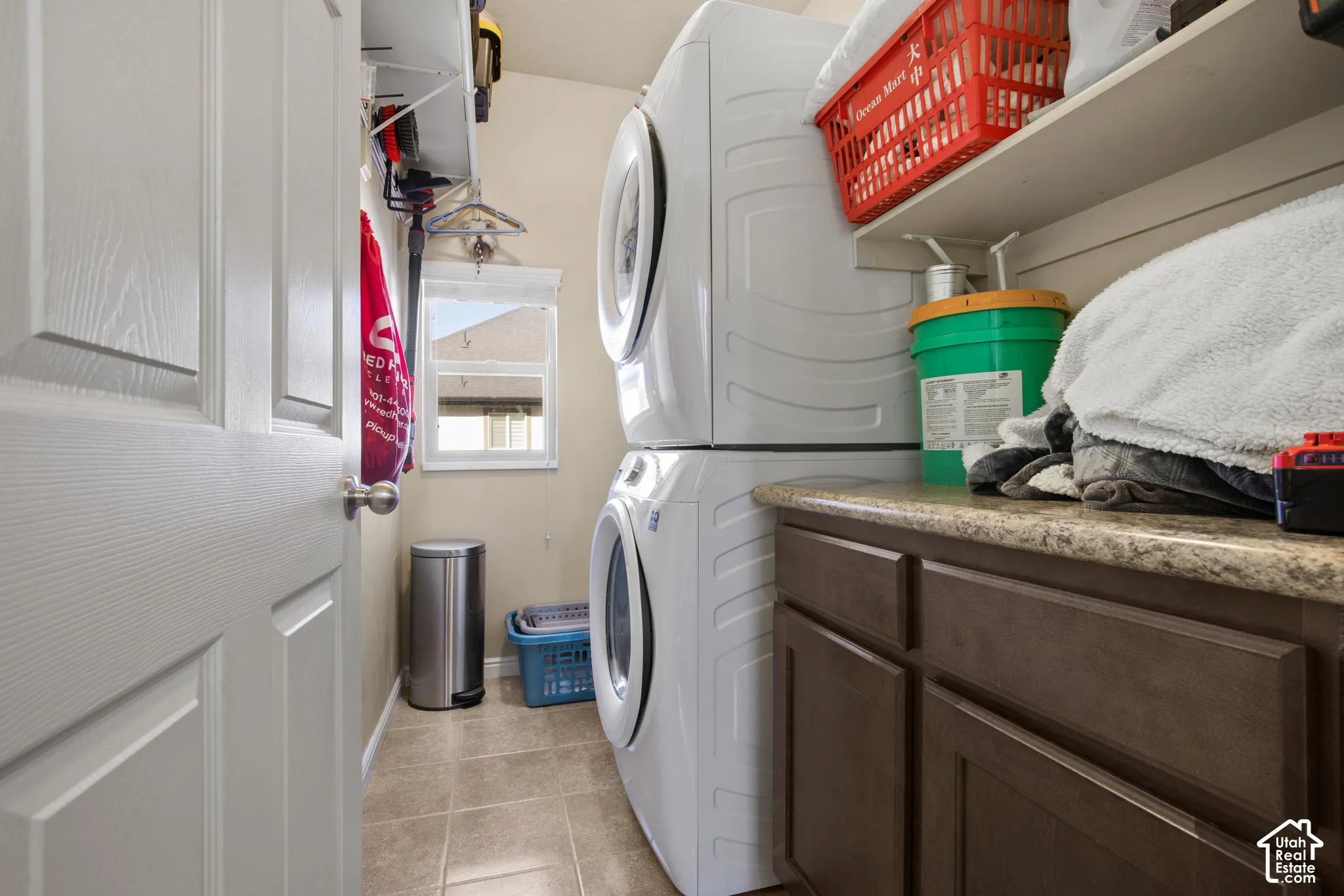 Laundry area featuring stacked appliances, built-in shelving, a window, brown cabinetry, and a countertop