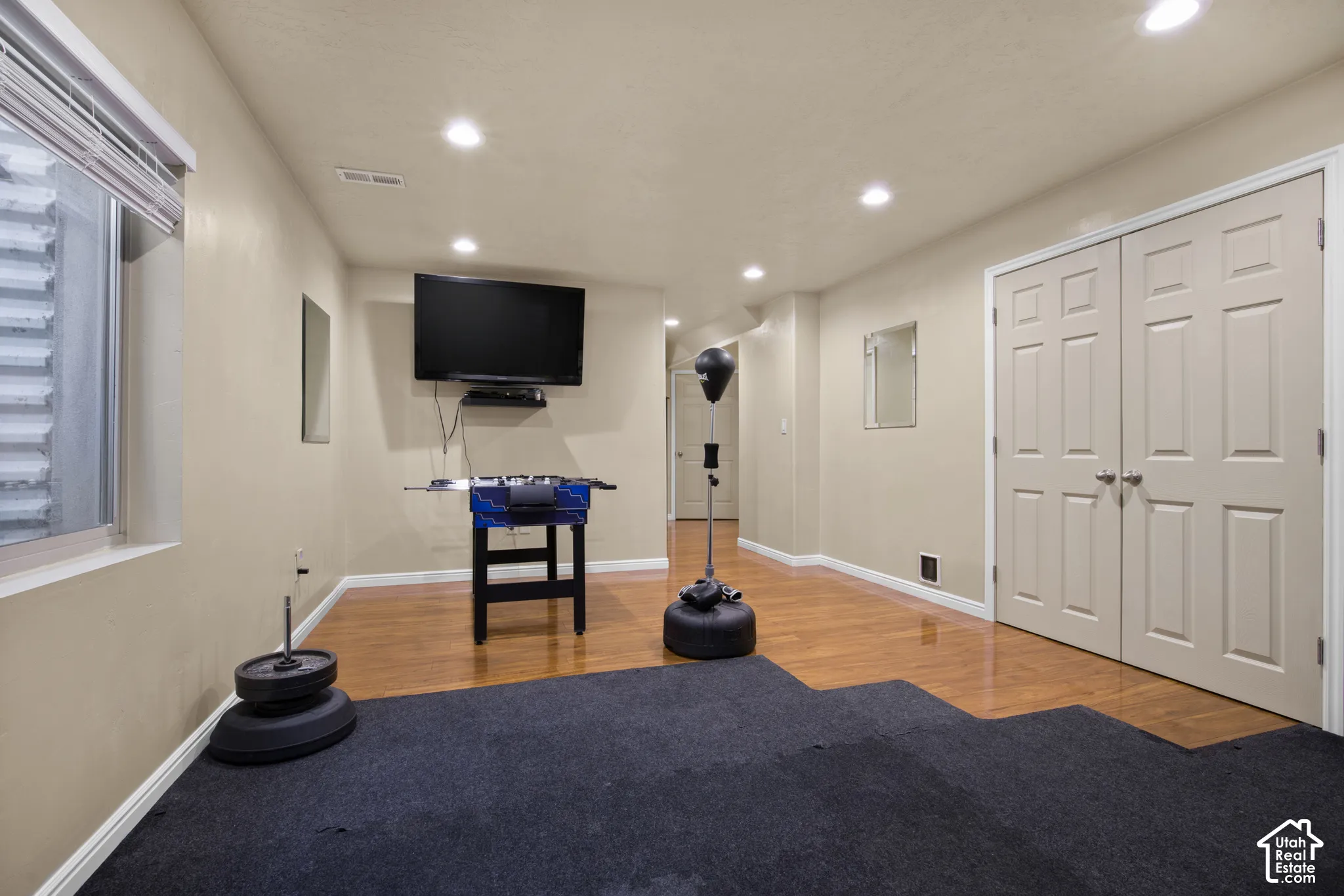 Lower-level room featuring recessed lighting, a window with blinds, wood-finish flooring, and a wall-mounted television