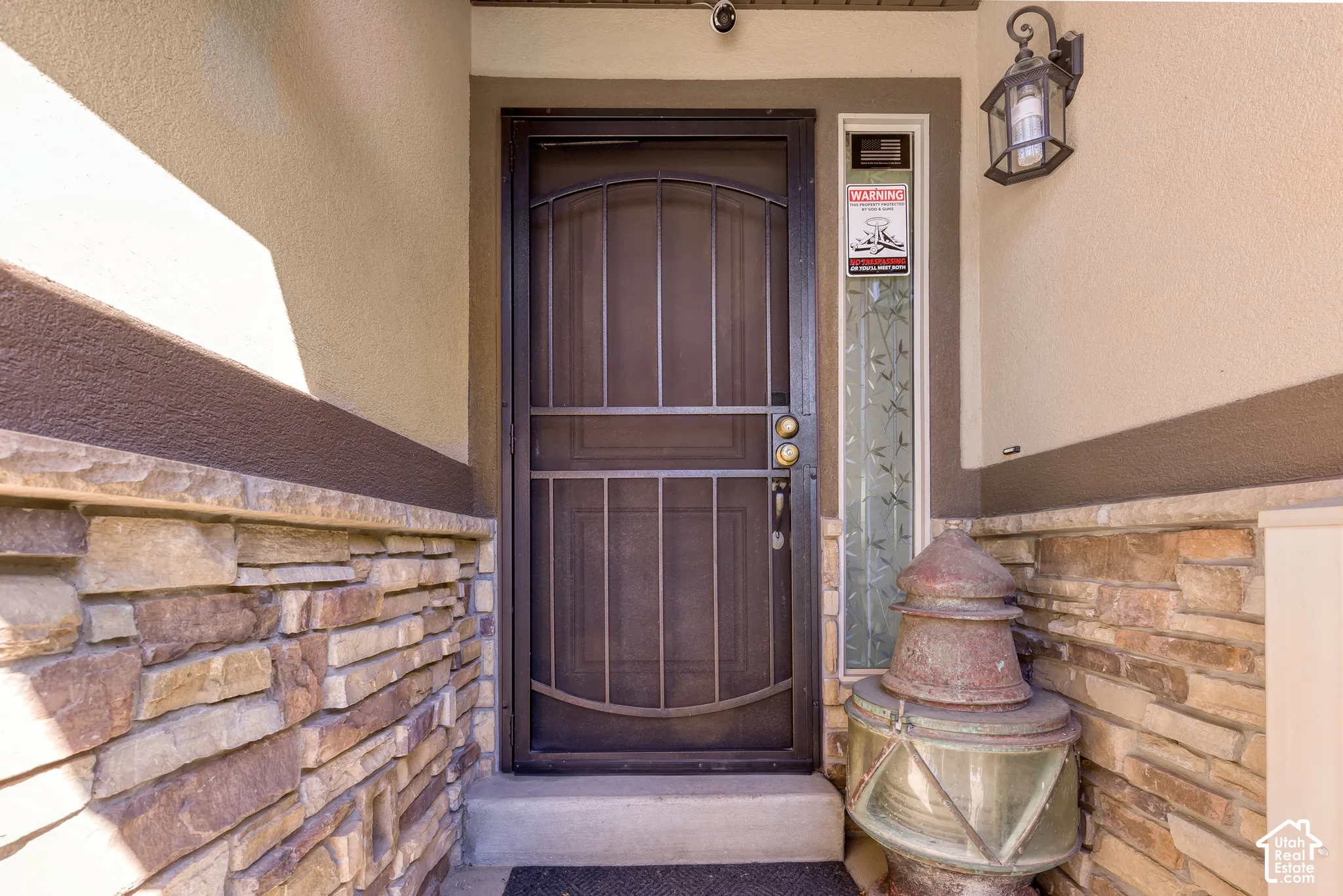 Entryway featuring a security screen door, stacked stone facade, textured stucco, decorative sidelight, and a wall-mounted exterior light fixture
