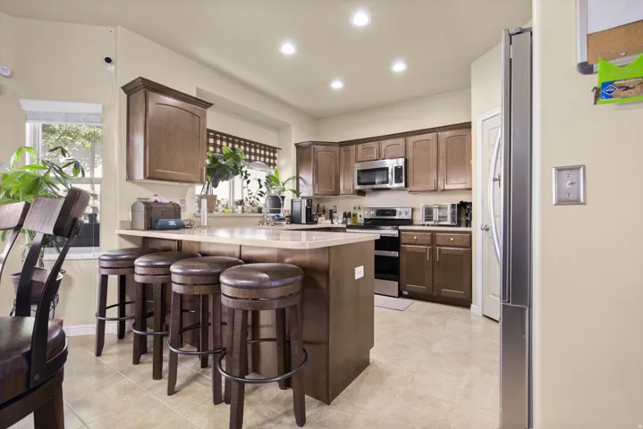 Kitchen featuring a breakfast bar with seating, recessed lighting, wood-finish cabinetry, stainless steel appliances, and light-toned tile flooring