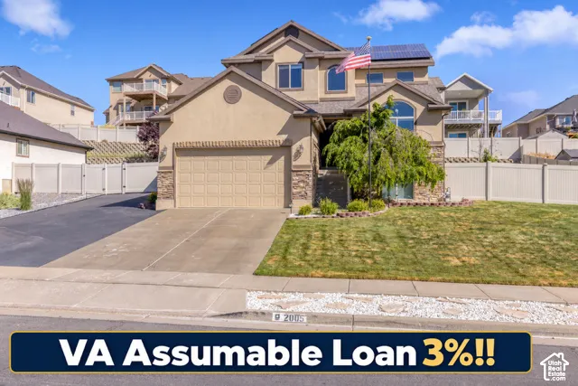 Multi-level exterior featuring stone and stucco siding, a two-car garage, roof-mounted solar panels, and a vinyl perimeter fence