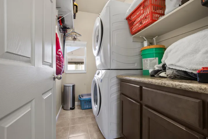 Laundry area featuring stacked appliances, built-in shelving, a window, brown cabinetry, and a countertop
