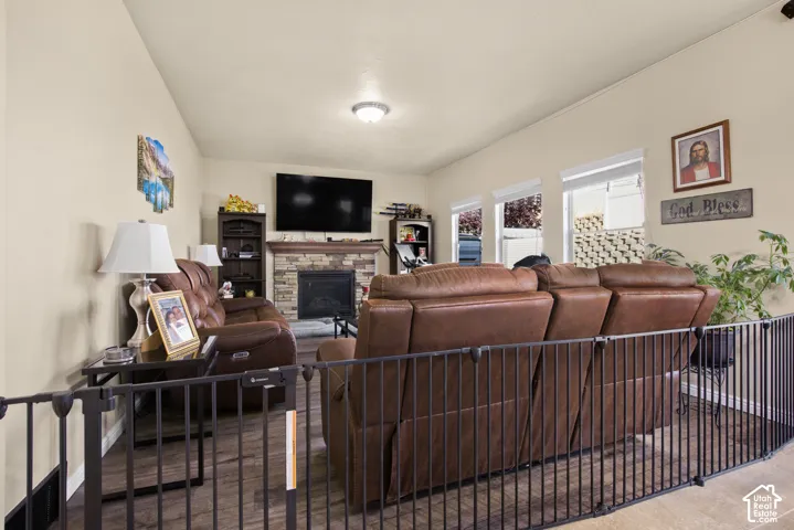 Living area featuring wood-finish flooring, a stone-faced fireplace, and a vaulted ceiling