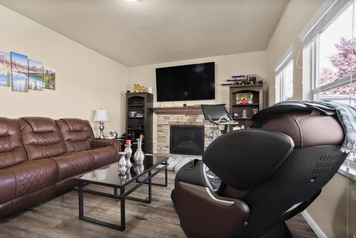 Living area featuring wood-finish flooring, a stone-faced fireplace with a mantel, and recessed lighting