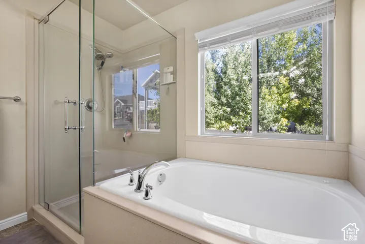 Built-in soaking tub with chrome fixtures, glass-enclosed shower with a handheld showerhead, and a large window providing natural light