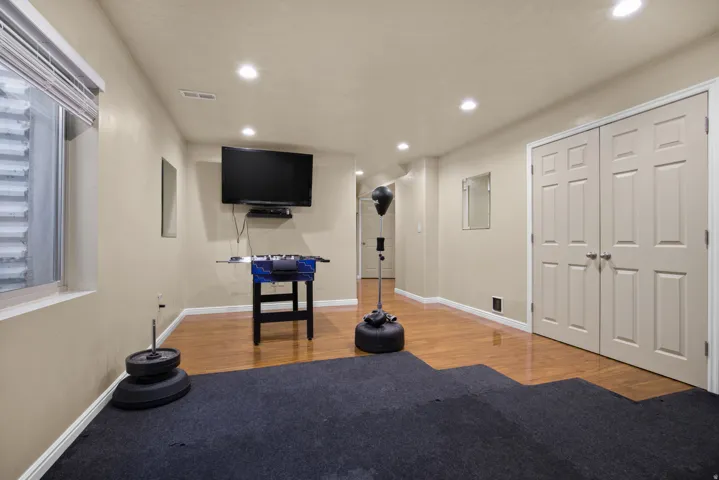 Lower-level room featuring recessed lighting, a window with blinds, wood-finish flooring, and a wall-mounted television