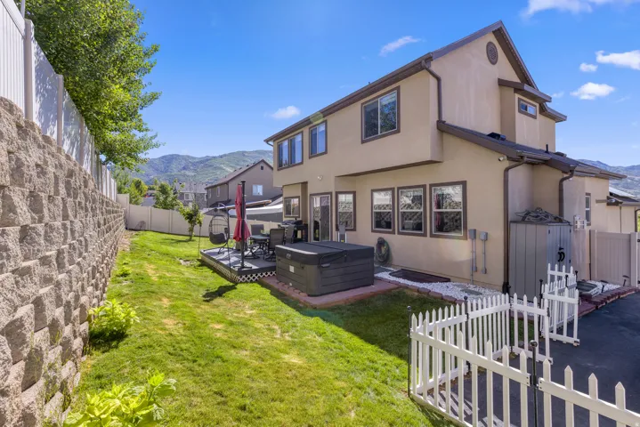 Rear exterior featuring a two-story stucco finish, multiple windows, and a raised wooden deck with a spa