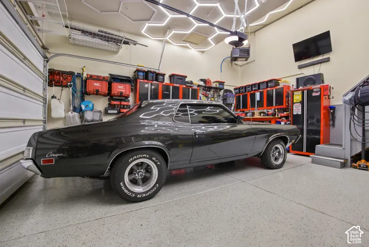 Spacious garage featuring a durable epoxy floor, integrated overhead storage, wall-mounted cabinetry, a built-in television, and bright overhead hexagonal lighting