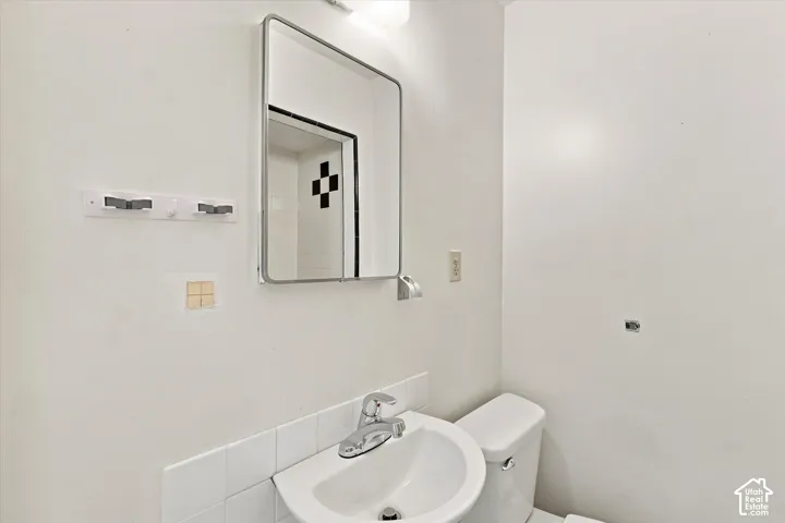 Wall-mounted mirror with integrated lighting, pedestal sink with chrome faucet, and white tiled backsplash