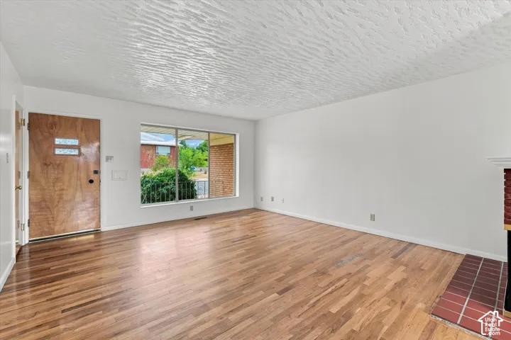 Wood-finish flooring, a wood front door with frosted glass inserts, a large picture window, and a brick fireplace