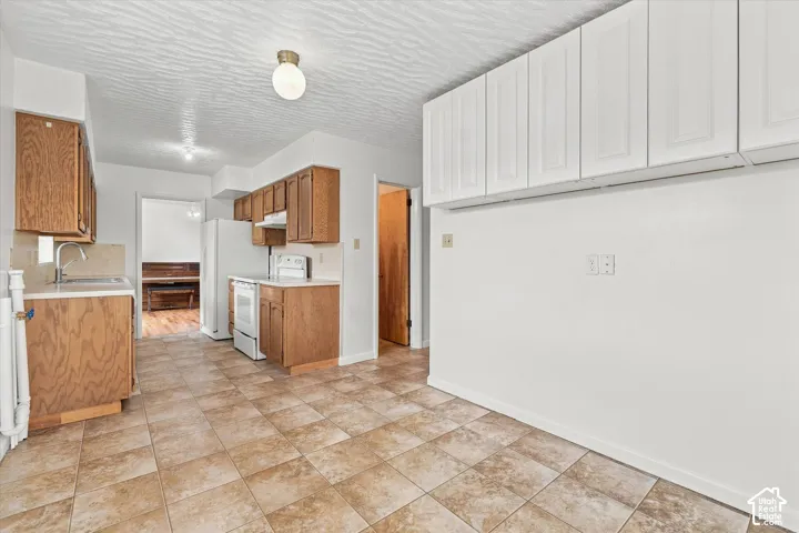 Kitchen featuring tile flooring, white appliances, wood-finish cabinetry, and overhead lighting