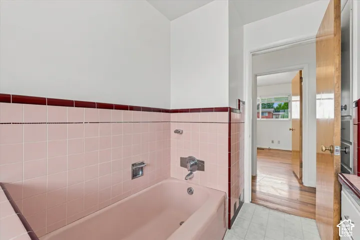 Bathroom featuring pink tile wainscoting with a red accent border, a built-in bathtub, and a tile floor