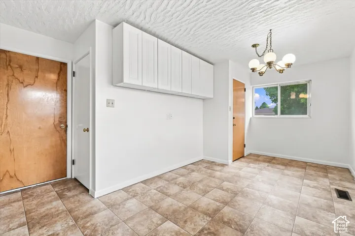 Tiled flooring, white walls, overhead cabinetry, window, and a chandelier-style light fixture