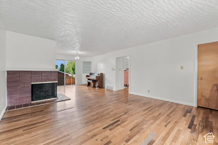 Spacious open-concept living area featuring warm wood-finish flooring throughout, white walls, and abundant natural light