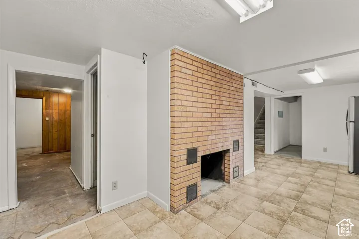 Brick fireplace with an open hearth, square tile flooring, painted white walls, and recessed lighting