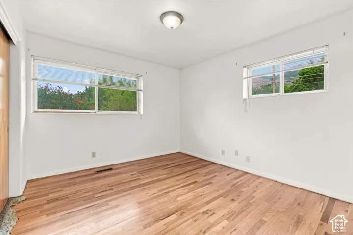 Hardwood flooring, white painted walls, two windows with blinds, and a flush mount ceiling light fixture