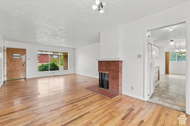 Wood-finish flooring, brick fireplace, large picture window, and a wood-finish entry door