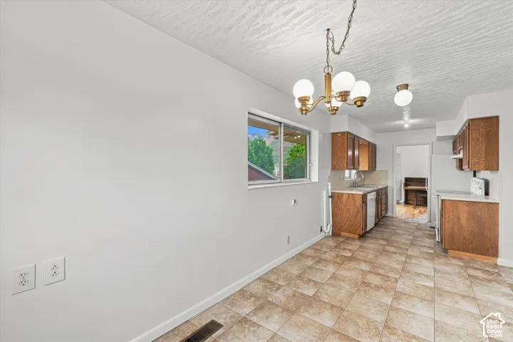 Kitchen space featuring a brass chandelier, wood cabinetry, built-in dishwasher, and tile flooring