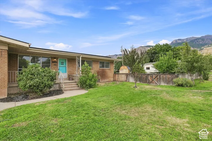 Brick exterior with multiple windows, front porch with railing, concrete steps, and a turquoise front door