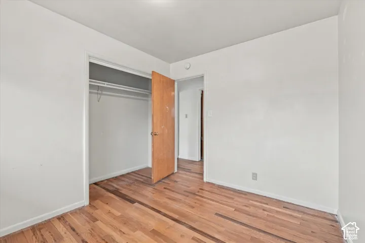 Wood-finish flooring with white baseboards, a built-in closet with a wooden door, and a white ceiling