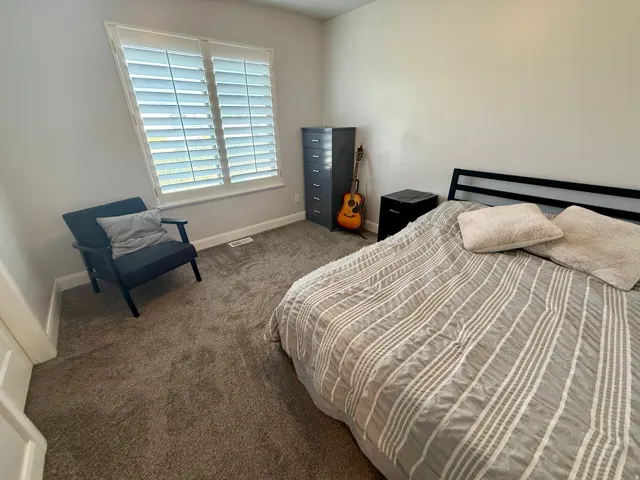 Bedroom featuring neutral wall paint, plush carpeting, a window with plantation shutters, white baseboards, and a white door frame