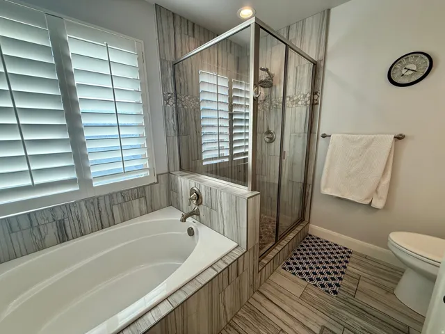 Bathroom featuring a built-in soaking tub and a glass-enclosed shower with stone tile surround