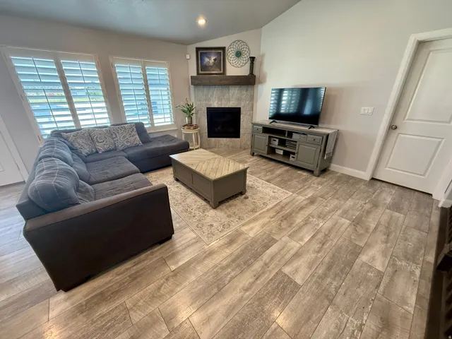 Living area featuring wood-finish tile flooring, a fireplace with a stone surround and wood mantel, and large windows with plantation shutters