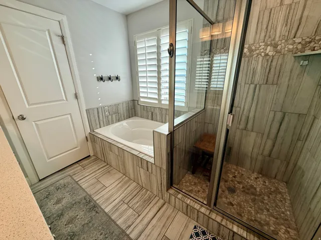 Bathroom featuring a glass-enclosed shower, a built-in tub, and plantation shutters