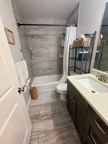 Bathroom featuring a white tub, shower with light-toned rectangular tile surround, dark wood-finish vanity with a light speckled countertop, undermount sink, and brushed nickel faucet