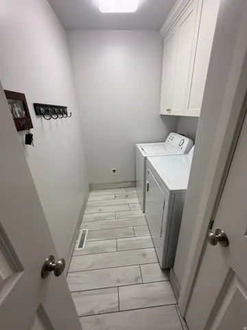 Dedicated laundry area featuring wood-finish tile flooring, white shaker cabinetry, and recessed lighting