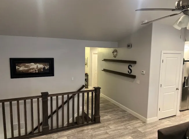 Upper level area featuring wood-finish flooring, a dark wood newel post and balusters, and a ceiling fan with light kit