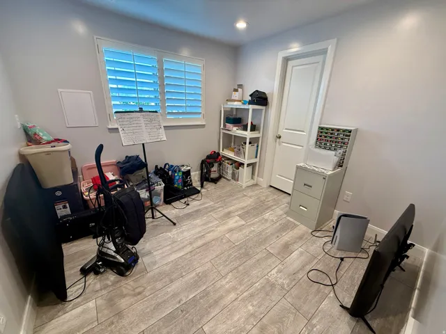 Room featuring wood-finish flooring, a window with white louvered shutters, a white paneled door, and recessed lighting
