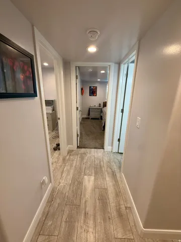Hallway featuring wood-finish flooring, recessed lighting, white baseboards, and neutral wall tones