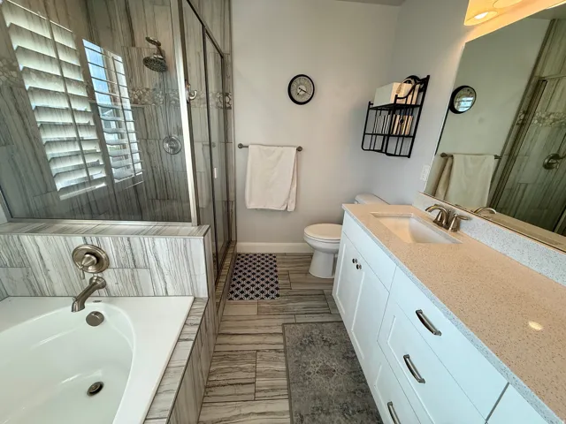 Contemporary bathroom featuring a built-in soaking tub with brushed nickel fixtures, a glass-enclosed shower with tile surround, a single vanity with a solid surface countertop, and wood-look tile flooring