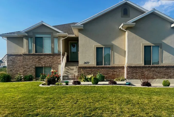 Stucco and brick facade residence featuring a prominent front entrance with stone steps, a manicured lawn, and planted garden beds