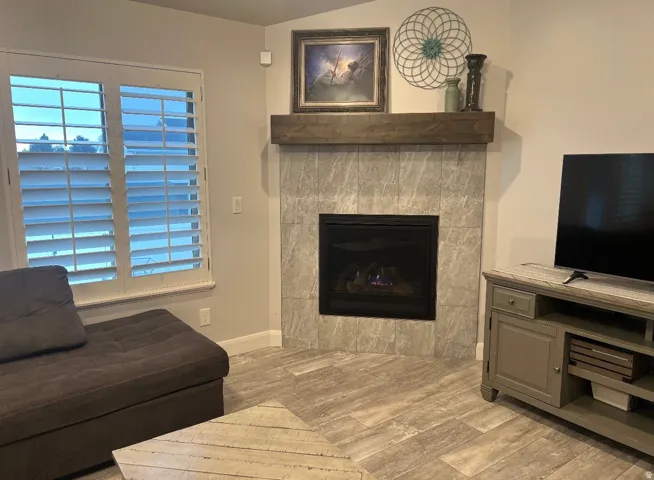 Corner fireplace featuring light gray tile surround and a wood-finish mantel